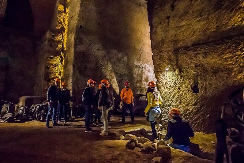 Napoli Sotterranea Gruppo di persone esplora una grotta, indossando caschi di sicurezza arancioni.